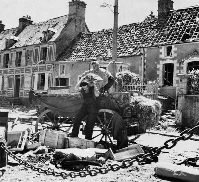 Two French civilian refugees from the battle that raged in St. Sauveur as American troops advanced on Cherbourg, 1944, unload their cart after returning to their homes.