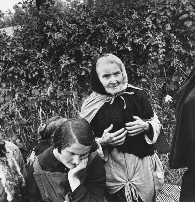 An aged French woman, who fled from her home when the allies launched their attack on the Normandy peninsula of France, waits at a roadside with other refugees for the tide of war to pass so they can return to their homes, 1944.