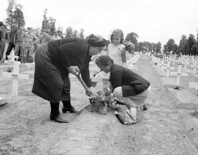 A French family living in the La Cambe area of Normandy, France, 1944, place flowers on the graves of the U.S. dead as part of the Bastille Day celebrations.