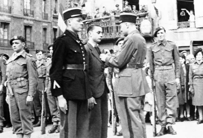 The gendarme (left center) who led the first British troops into Bayeux, and a French underground leader, center, are decorated with the Croix de Guerre during Bastille Day ceremonies in a French city on the Normandy coast, France, 1944.