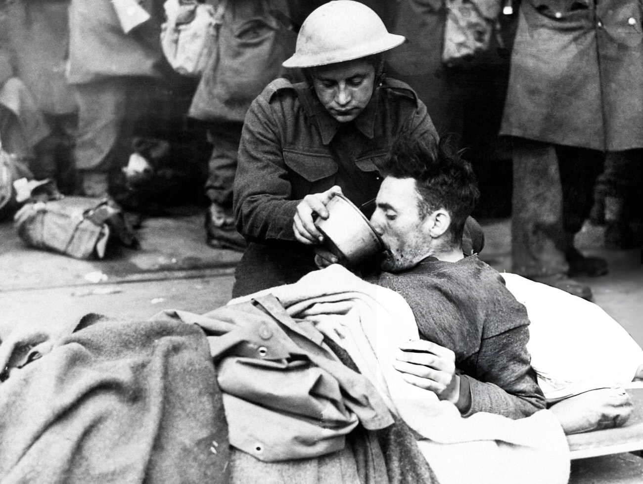 A British soldier helps a wounded man drink while waiting to be evacuated from Dunkirk, France, 1940.