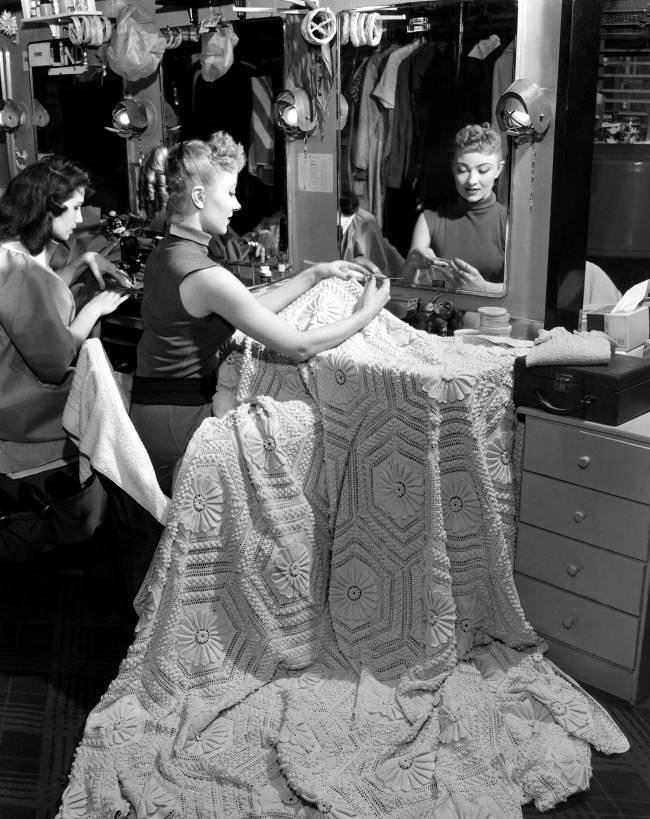 Jane Freund crochets a bedspread while a fellow dancer sews at a machine in one of dressing rooms backstage of Radio City Music Hall, 1958.