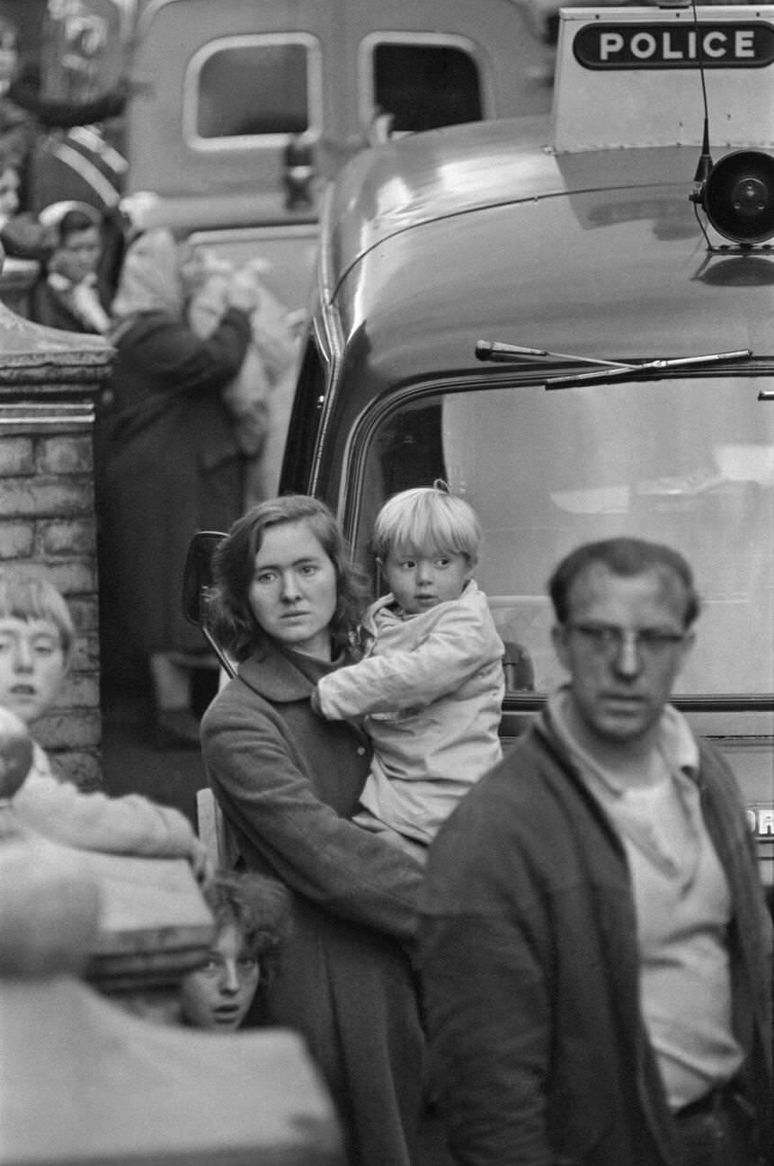 Local villagers, including a young mum carrying her child, are shocked and look on in bewilderment as the rescue effort at the Pantglas Junior School carries on, 1966.