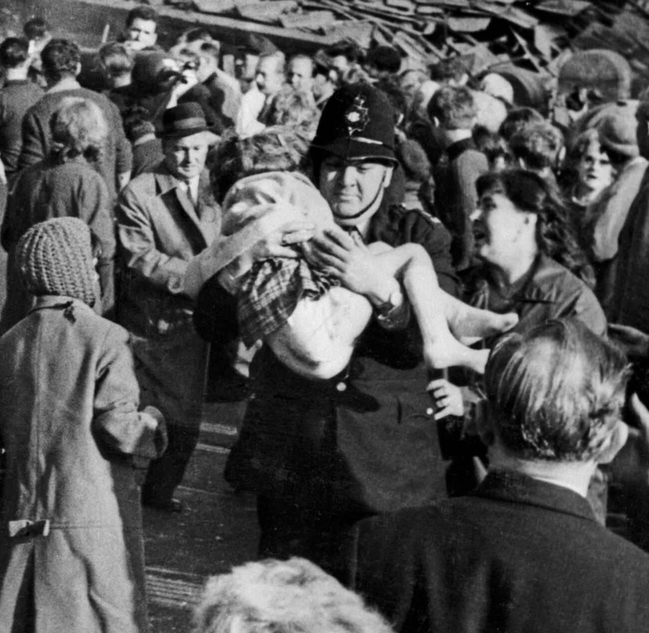 Policeman Victor Jones carries a little girl from the wrecked school as woman anxiously looks to see if she can recognise her, 1966.