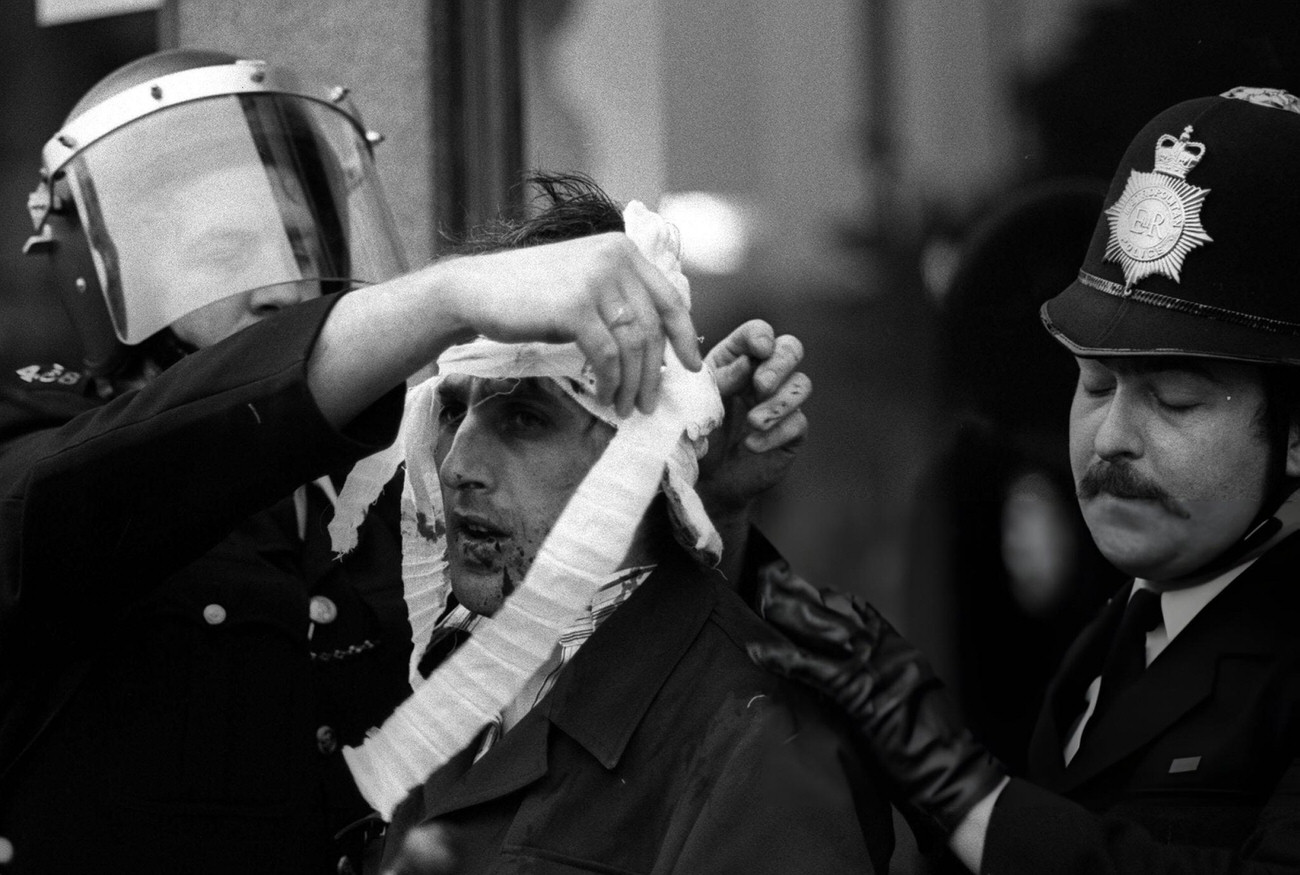 A policeman in a riot helmet bandages an injured man at Brixton, South London, during an anti-racial rioting demo.