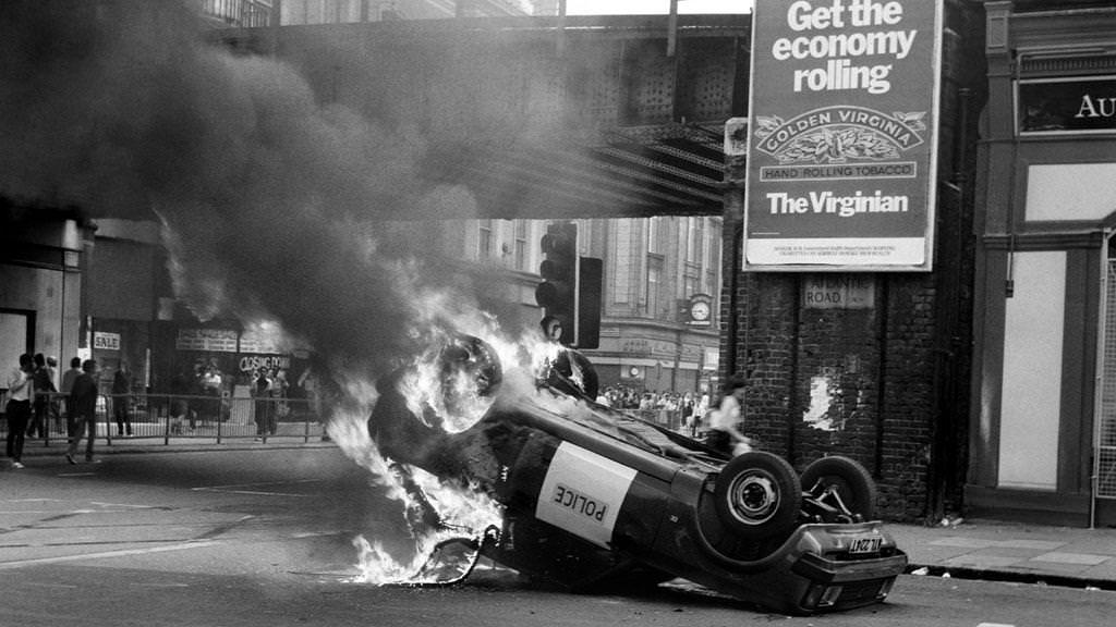 A police car blazes at the corner of Atlantic Road and Brixton Road in Brixton, South London, 1981.