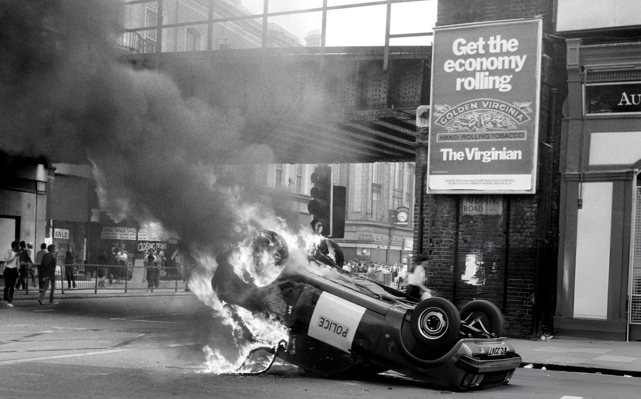 A police car blazes at the corner of Atlantic Road and Brixton Road, Brixton, South London, 1981.