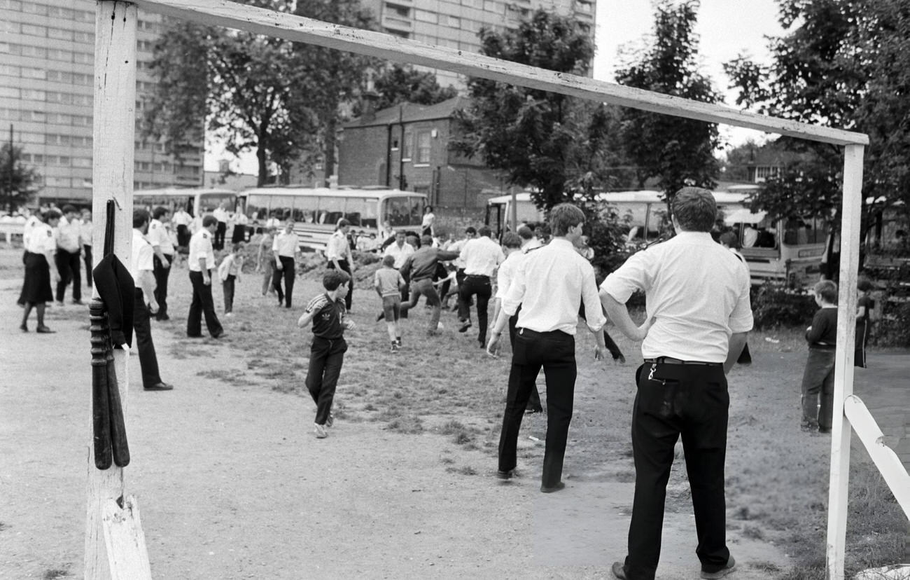 Policemen and women on riot stand-by in Bow, East London, pass the time playing football with local children. The officers had got out of their coaches, hung up their truncheons up on the goalposts and kicked-off, 1981.