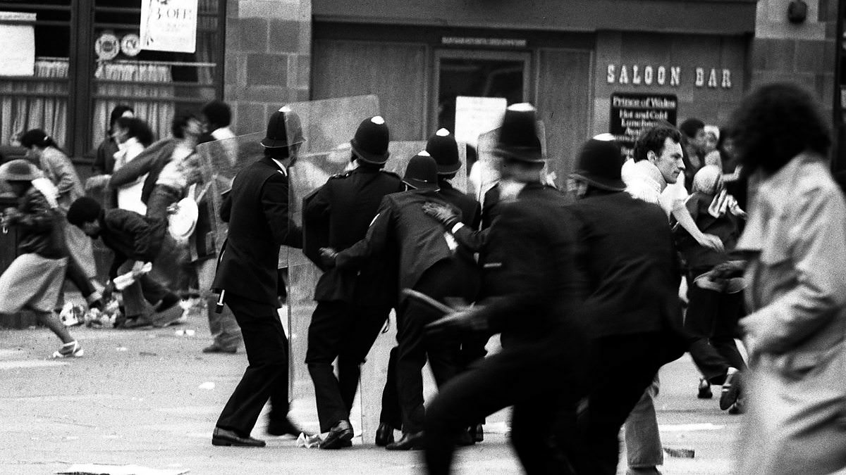 Armed with riot shields, police huddle together for protection as violence flared near Lambeth Town Hall in Acre Lane, Brixton, South London. Rioters smashed shop windows in the Brixton Road and began looting. Police squads moved in on foot and by van, 1981.