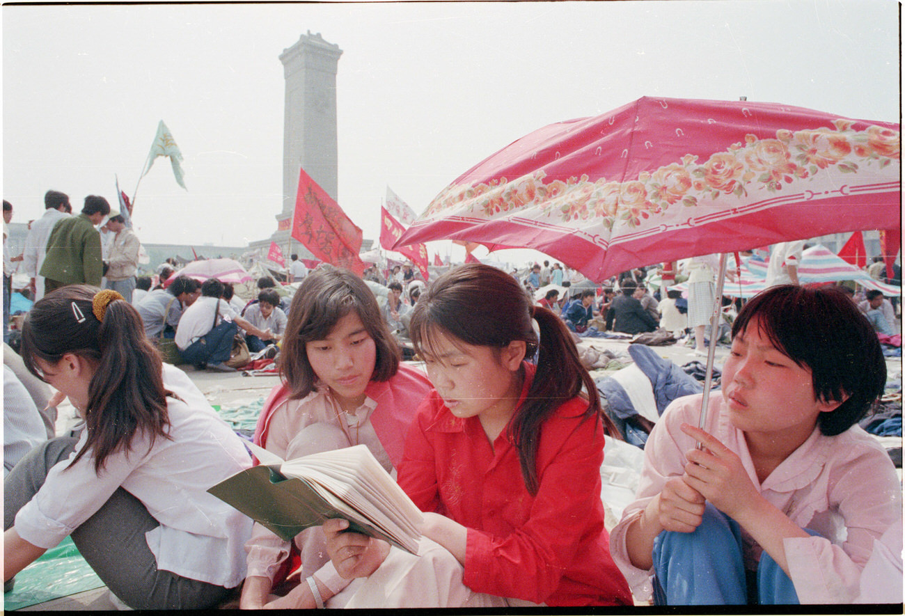 A group of young Chinese women read together in Tiananmen Square.