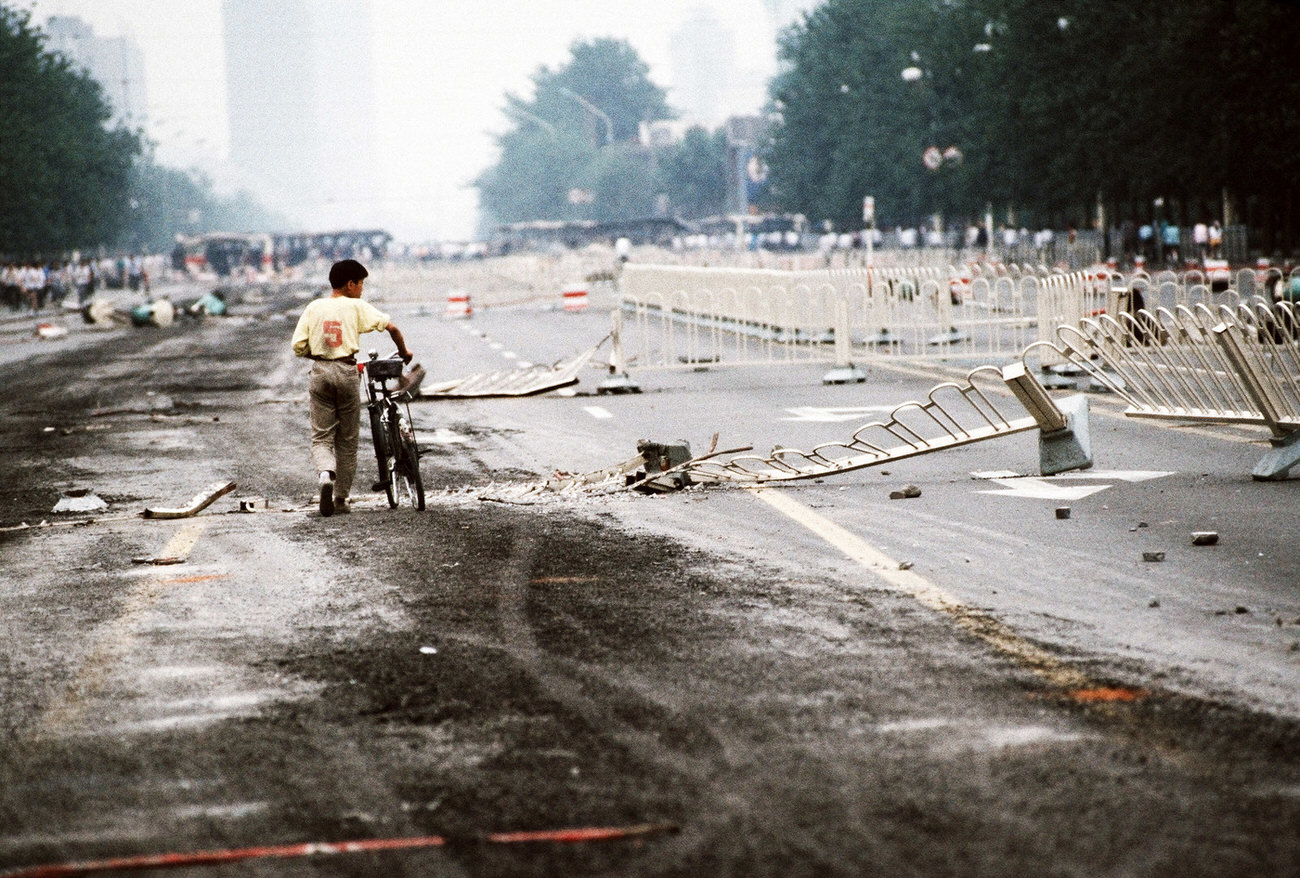 A lone cyclist walks past street barriers on Changan Avenue that have been crushed by Chinese army tanks during the night of violence in and around Tiananmen Square.