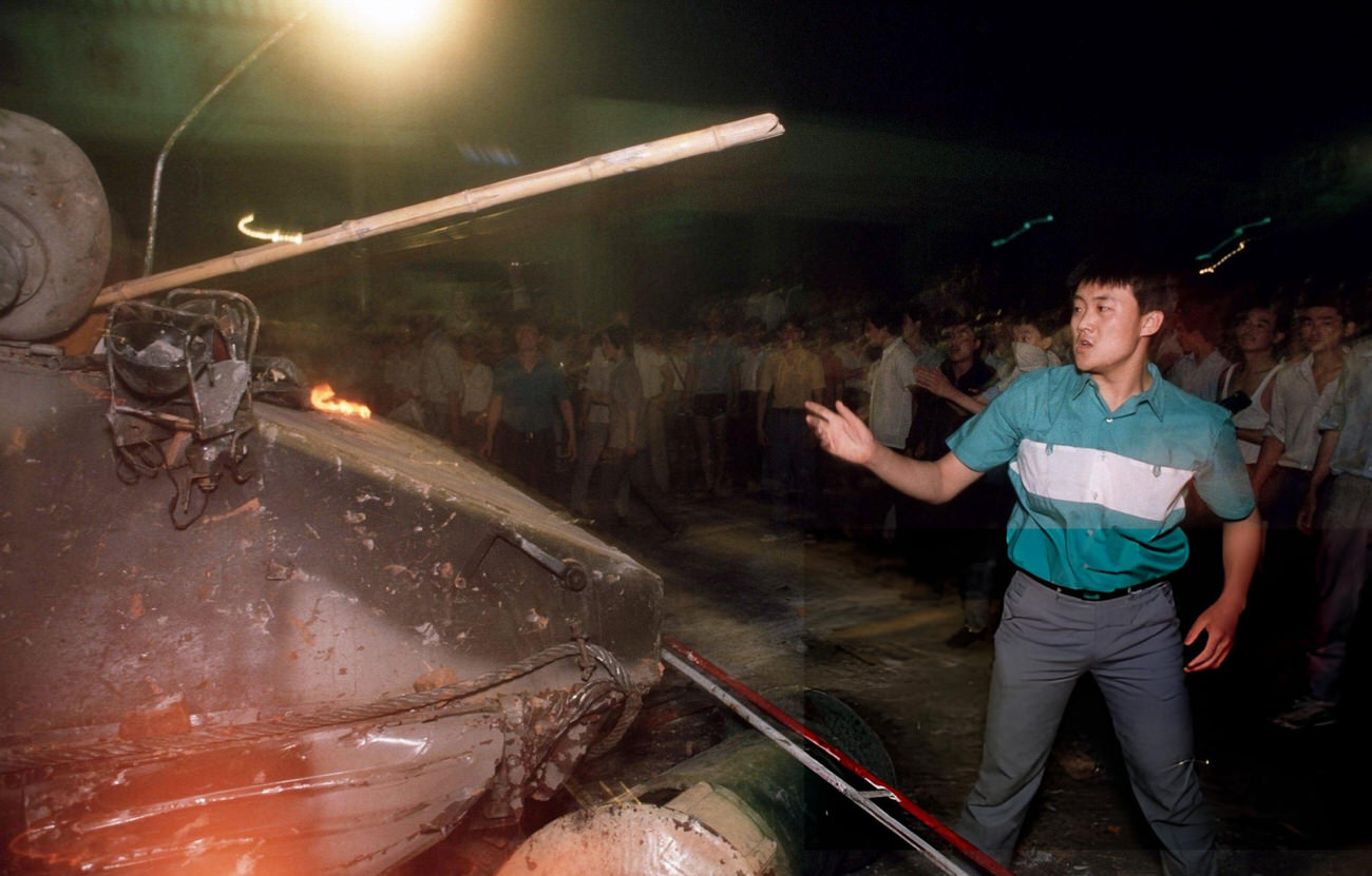 A pro-democracy demonstrator throws a wood pole at a burning armored personnel carrier, 1989.