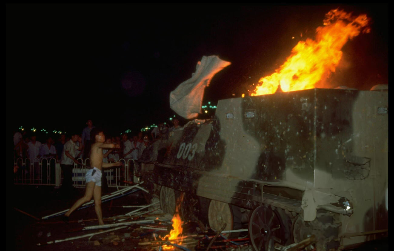 A man in shorts hurls white cloth at a burning tank, 1989.