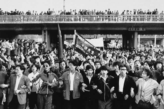 Jubilant student marchers, arms lined, pass under a bridge lined with local supporters, Thursday, April 27, 1989, Beijing, China. Students in the ten of thousands from several Beijing schools demonstrated in defiance of a government ban.