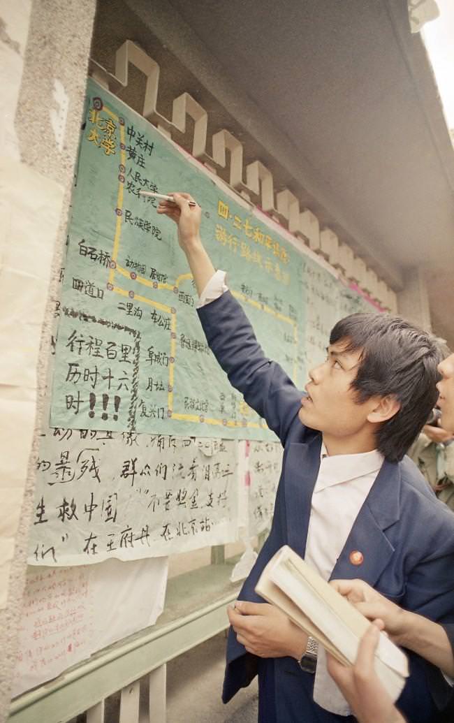 A student at Beijing University points to a map of the march route on a poster up on campus as he recounts a tale of how marchers pushed through police lines on their way to Tiananmen Square, April 28, 1989.