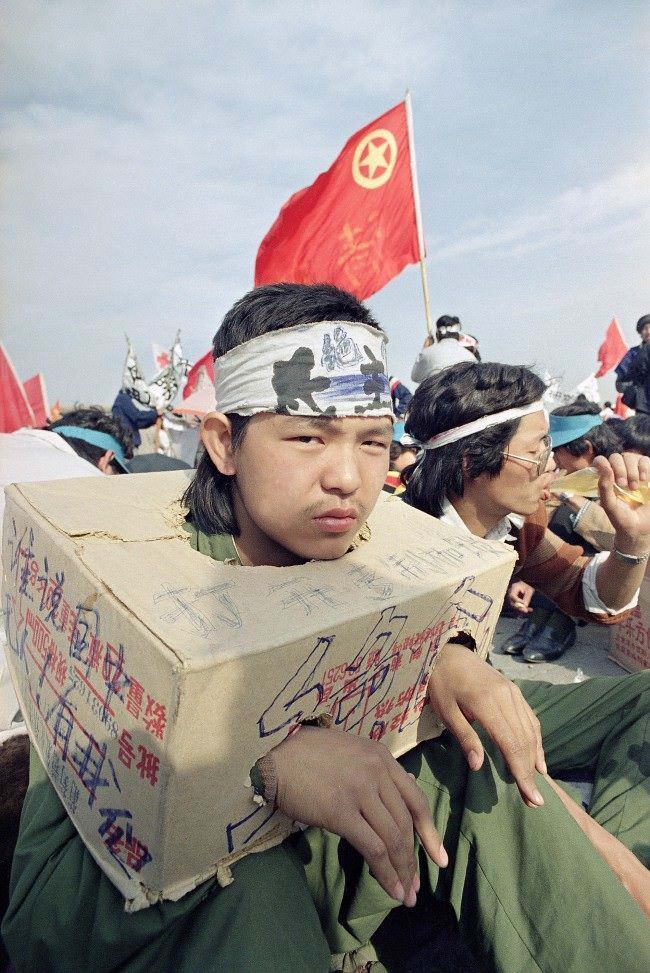 A Beijing university student sits bound in a cardboard box as the strike for democracy continues for the third day in Beijing’s Tiananmen Square, Tuesday, May 16, 1989. The box indicates he cannot use his hands so he cannot eat.