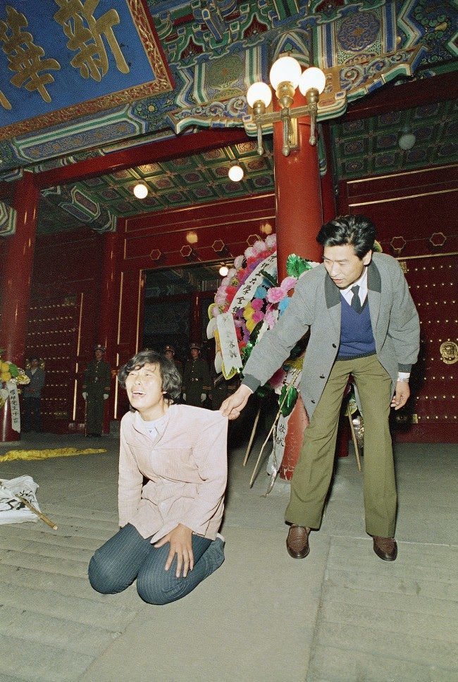 A Chinese security guard gently tries to move a weeping young woman away from the ornate entrance to the Chinese Communist Party headquarters, Zhongnanhai, early on Wednesday, April 19, 1989 in Beijing. University students converged on Zhongnanhai after demonstrating in Tiananmen Square all day on Tuesday. The students tried to storm the gate, but were fought back by Chinese security.