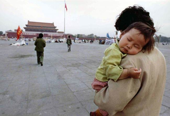 A child sleeps on his mother’s shoulder as she crosses Tiananmen Square, Beijing, on May 29, 1989. Many students have tired and returned to their classes following three weeks of pro-democratic rallies.