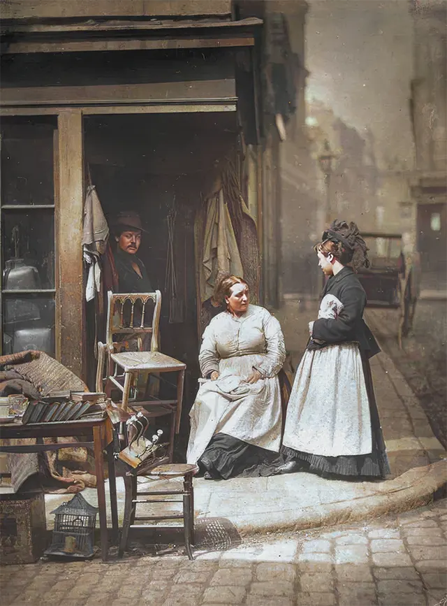 Women talk outside a secondhand shop in London, 1890s.