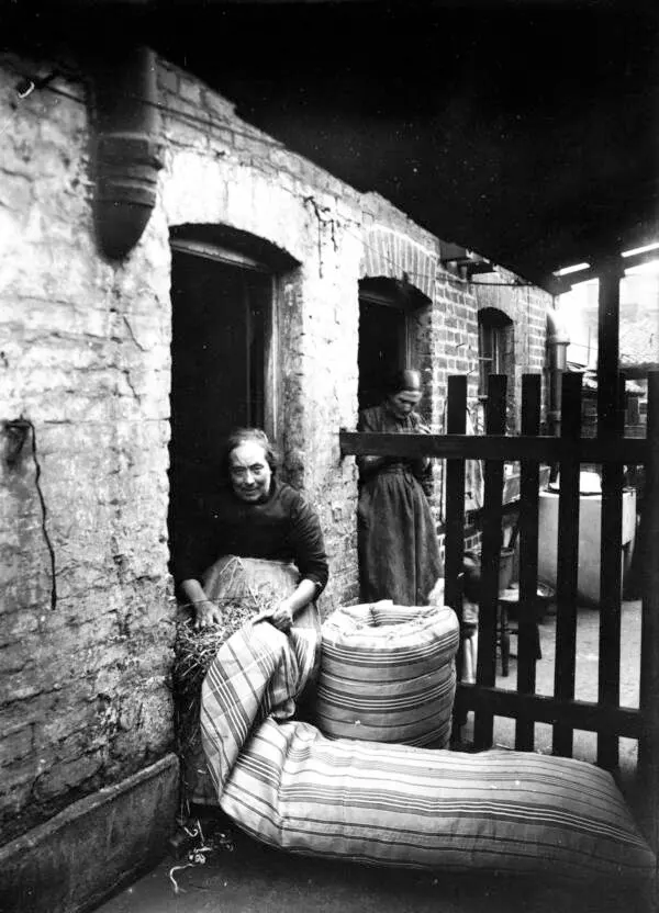 A woman identified as Ma Rolinson making a mattress in the slums of Bethnal Green. 1890s.