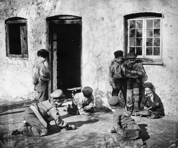 Children gather in the yard in London’s slums to play a game of marbles. 1860.