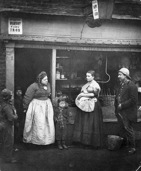 In this 1877 photograph, Londoners affected by flooding stand in front of a rag shop.