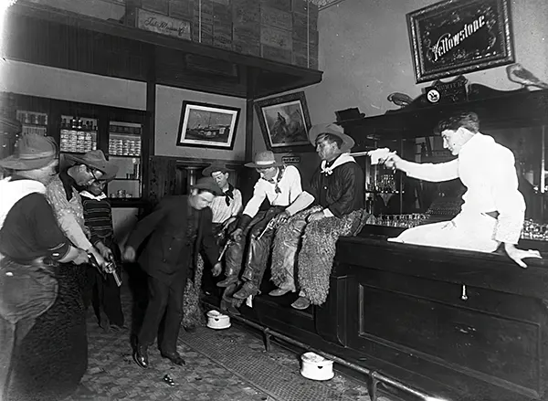 At an unspecified saloon, possibly in Wyoming, patrons are seen apparently compelling a man to “dance” by pointing their guns at his feet, 1880s.