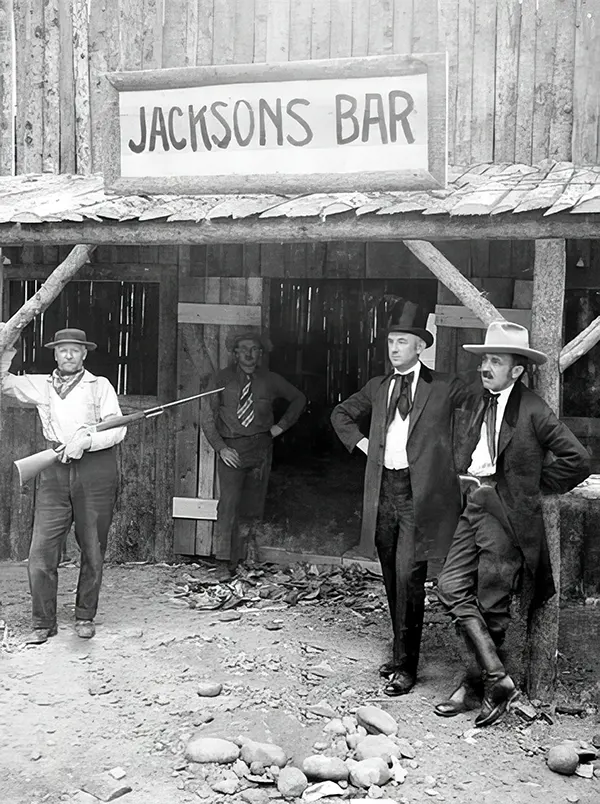 A patron cradles a rifle outside Jacksons Bar in Idaho, late 19th century.