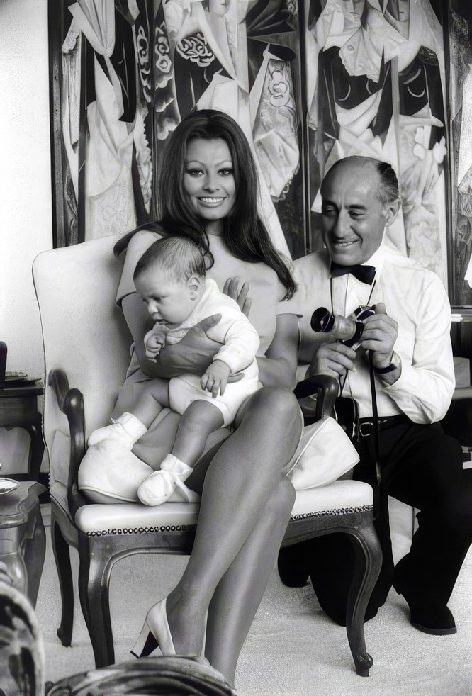 Sophia Loren holds her newborn son, Carlo Ponti Jr., in the bedroom of her Italian villa as Alfred Eisenstaedt crouches beside her, 1969.