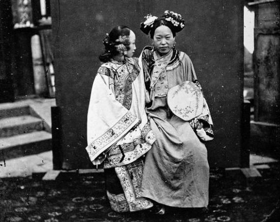 This Manchu bride is all decked out in her wedding finery, and both the ladies in the picture – taken in 1871 – are dressed in the Manchu style of curve-fronted robes that fastened at the shoulder.