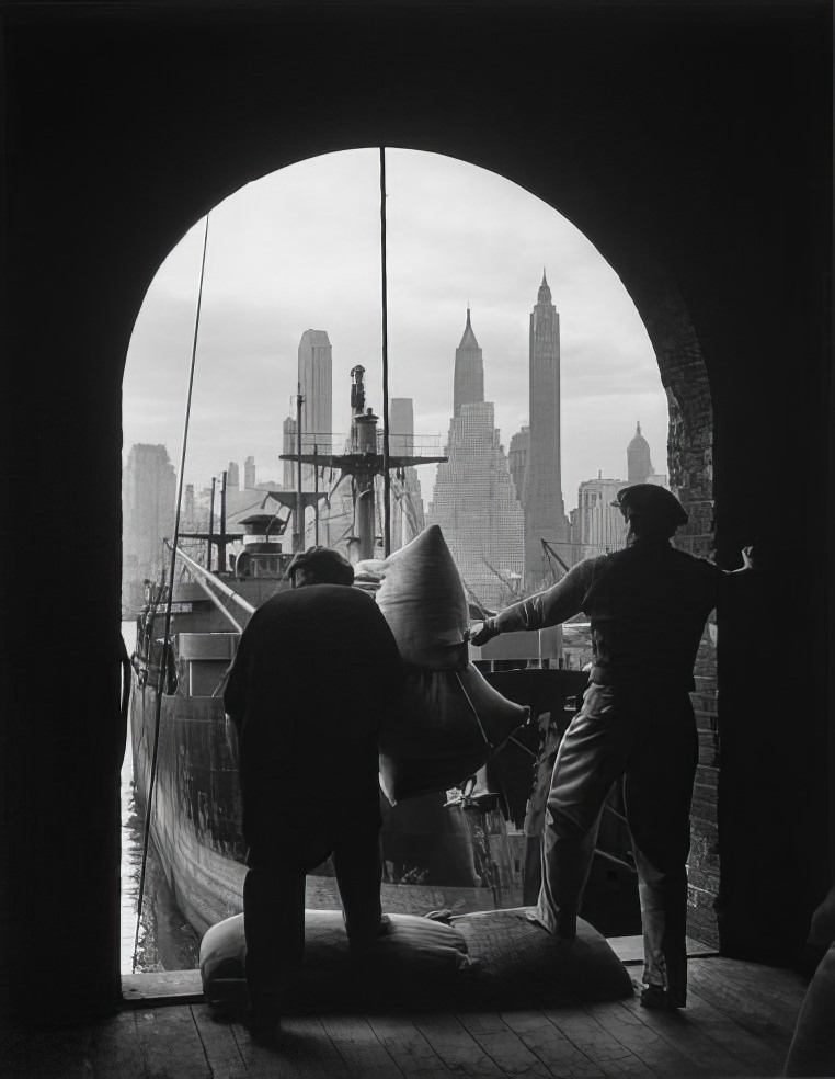 Men unload coffee at a Brooklyn dock with Lower Manhattan visible in the background, 1949