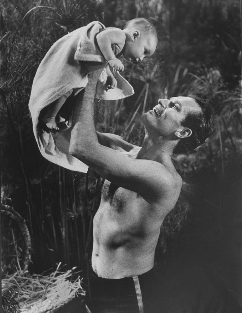 Charlton Heston lifts his two-month-old son, Fraser, who is portraying the baby Moses during filming of The Ten Commandments, 1955.