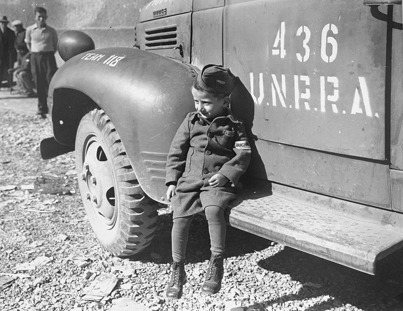 A four-year-old survivor of Buchenwald sits on the running board of an UNRRA truck soon after the liberation of the camp. , 1945.