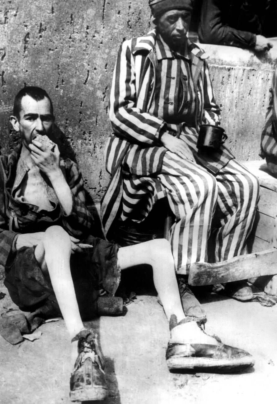 Two emaciated former prisoners lean against a wall while eating a loaf of bread after the liberation of the Buchenwald concentration camp, 1945.