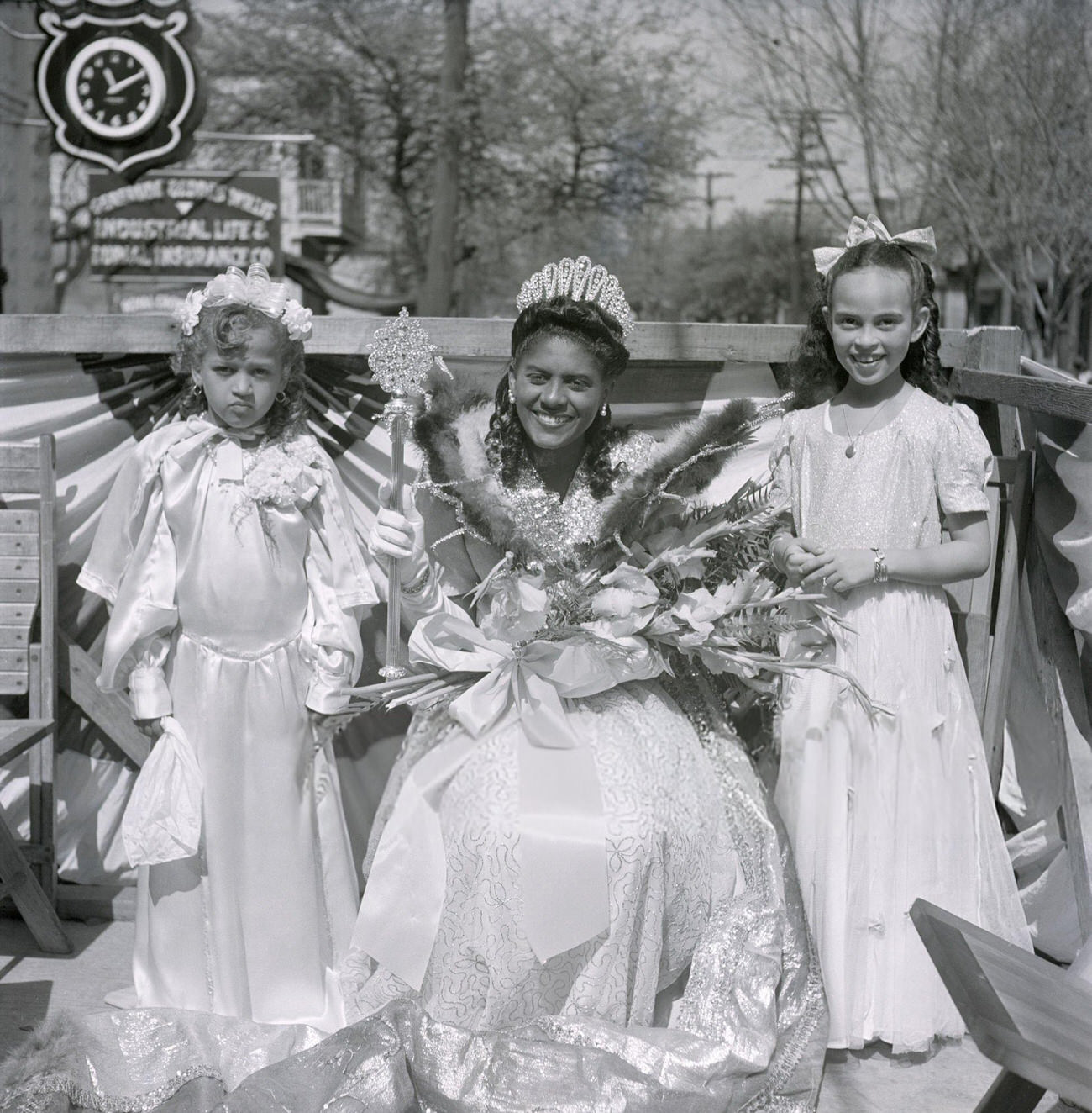 A Mardi Gras Princess and Two Younger Attendants Ride a Parade Float Wearing White Gowns and Holding Bouquets, 1950s.