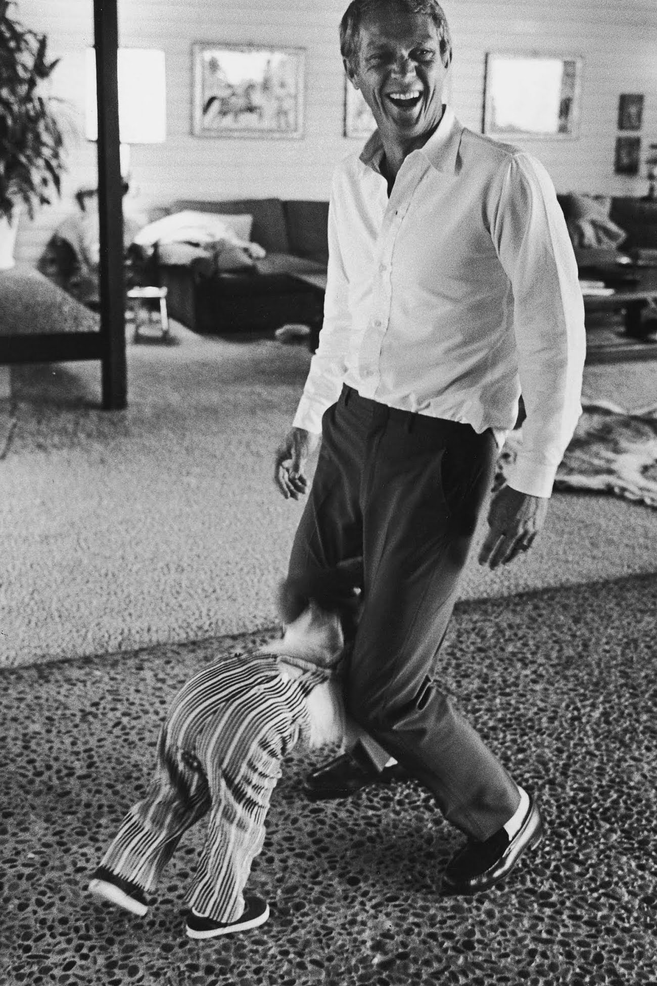 Steve McQueen laughing while playing with his son, Chad McQueen, 1963.