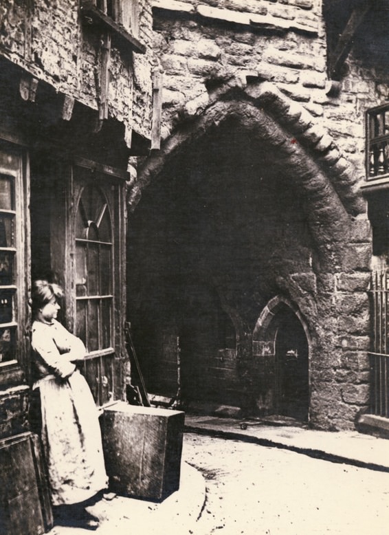 Black Gate, close-up of the gateway with a woman leaning against a shop doorway, 1880.