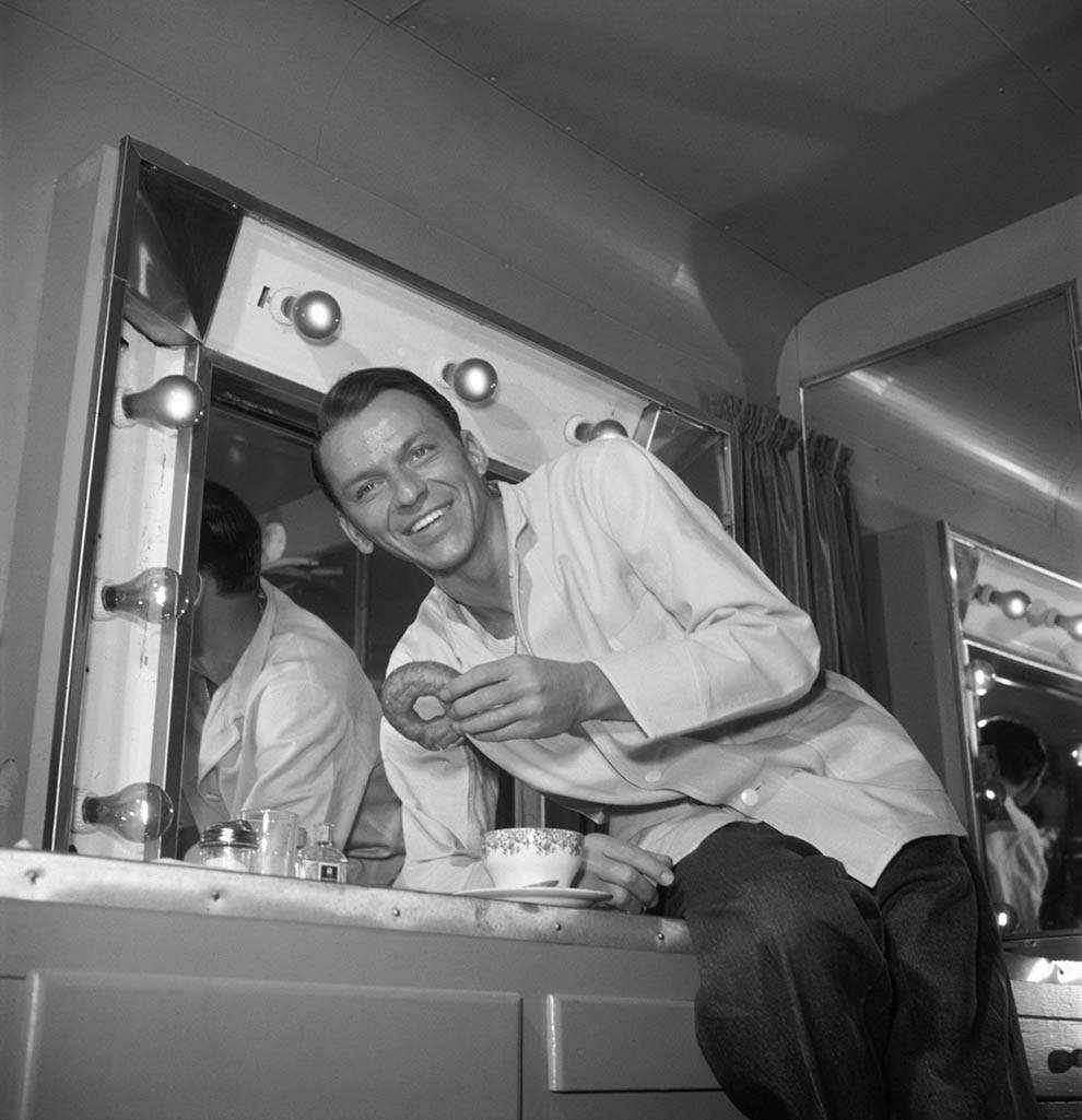 Frank Sinatra putting moves on a doughnut. In his trailer during a break in filming, circa 1950.