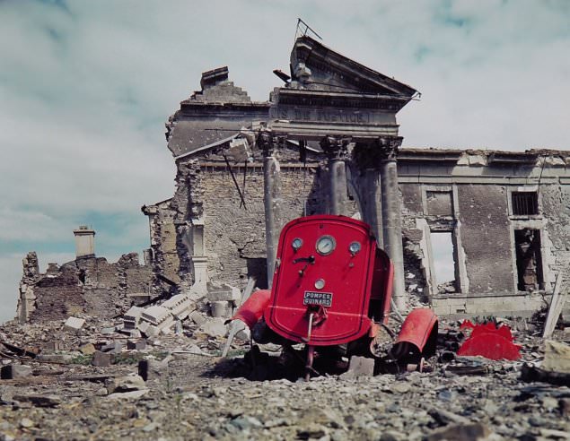 View of the ruins of the Palais de Justice in the town of St. Lo, France, summer 1944. The red metal frame in the foreground is what’s left of an obliterated fire engine