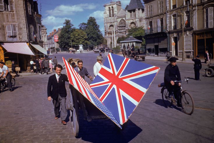 Frenchmen transport painted British and American flags for use in a parade, summer 1944