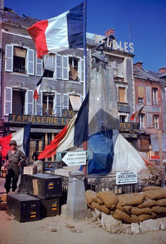 American troops stand beside a World War 1 monument bedecked with French flags after the town (exact location unknown) was liberated from German occupying forces, summer 1944