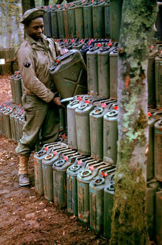 An American corporal stacks cans of gasoline in preparation for the upcoming invasion of France, Stratford-upon-Avon, England, May 1944