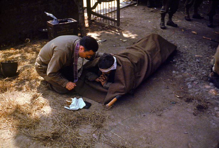 An American Army chaplain kneels next to a wounded soldier in order to administer the Eucharist and Last Rites, France, 1944