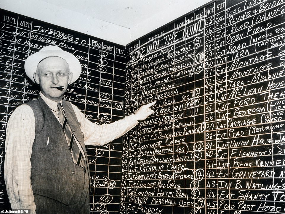 A technician on the set points to a board showing the different locations of the scenes in chronological order.