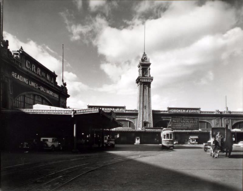 Lackawanna and Hoboken ferries, with clock tower above, C.R.R. of N.J. ferry, left, 14th St. trolley and cars and wagons.