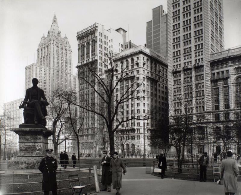 Madison Square, looking northeast, Manhattan. Policeman stands in front of Seward statue, shoe-shine man lounges on railing, right, Metropolitan Life building rises above park.