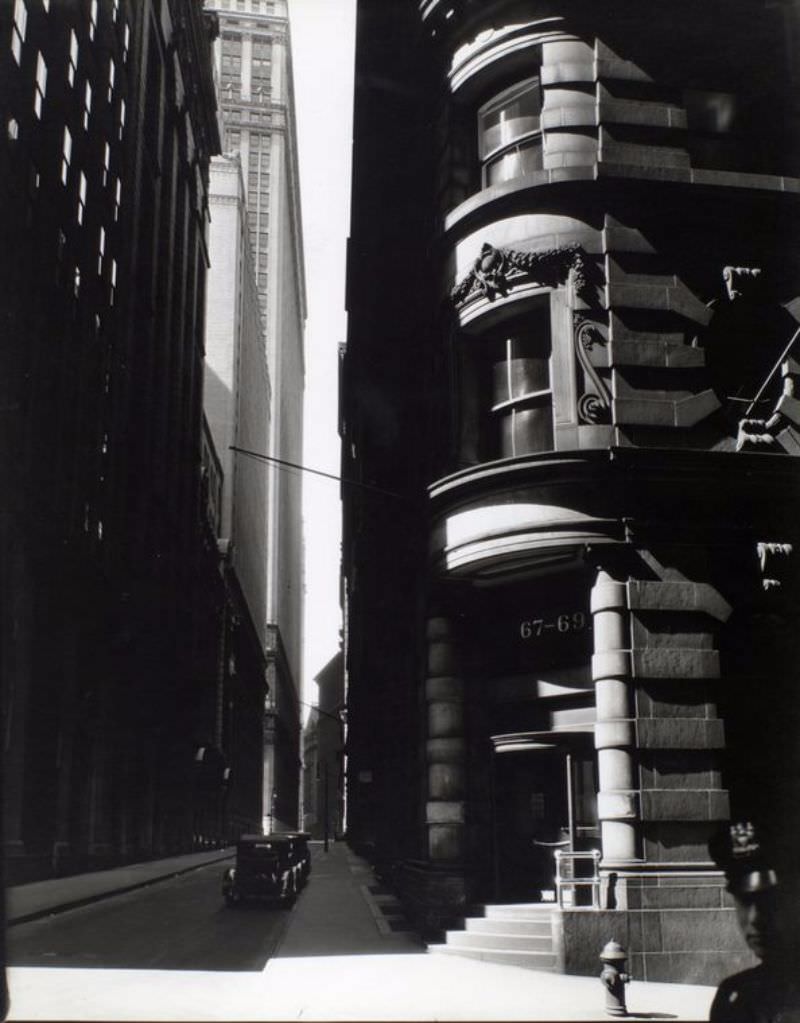 Looking down Cedar Street, in shadow, rounded corner and entrance of #67-69 at right, police officer just visible, lower right corner.