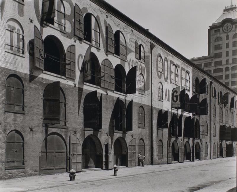 Warehouse, Water and Dock Streets, Brooklyn. Four-story brick warehouse with arched windows and doors, some of which are open, partially hiding the Yuban Coffee advertisement painted on it.