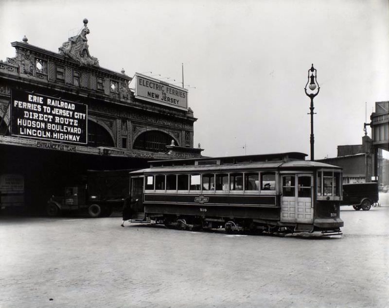 Woman boards 23rd St. trolley outside Erie Railroad Ferry terminal, West 23rd St., trucks, lamppost visible.