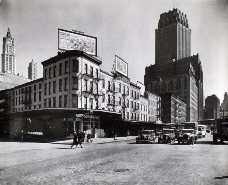 Billboards top buildings at the corner of Warren and West Sts., cars stopped in street, Telephone and World Telegram building beyond.